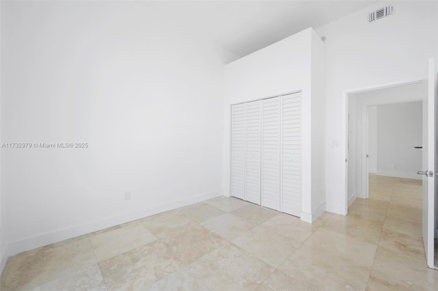 unfurnished bedroom with a high ceiling, a closet, visible vents, and baseboards