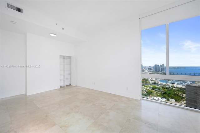 unfurnished room with a city view, a wall of windows, visible vents, and plenty of natural light