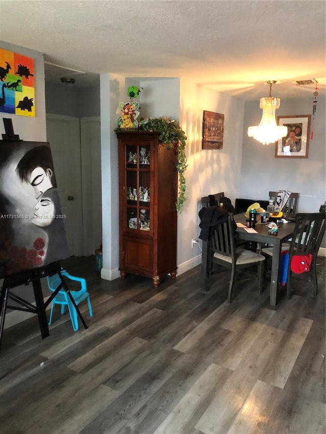 dining area with dark wood-type flooring, a textured ceiling, and a notable chandelier