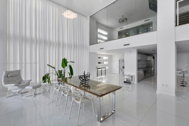 tiled dining space with a notable chandelier, a wealth of natural light, and a high ceiling