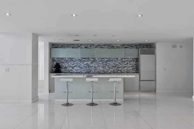 kitchen with built in refrigerator, gray cabinets, and a breakfast bar area