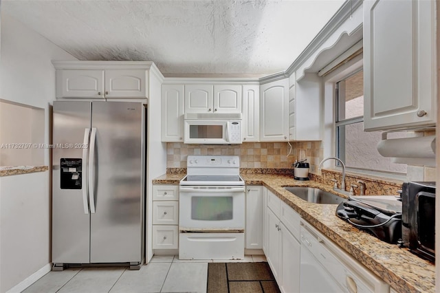 kitchen with light tile patterned flooring, sink, white cabinetry, light stone counters, and white appliances