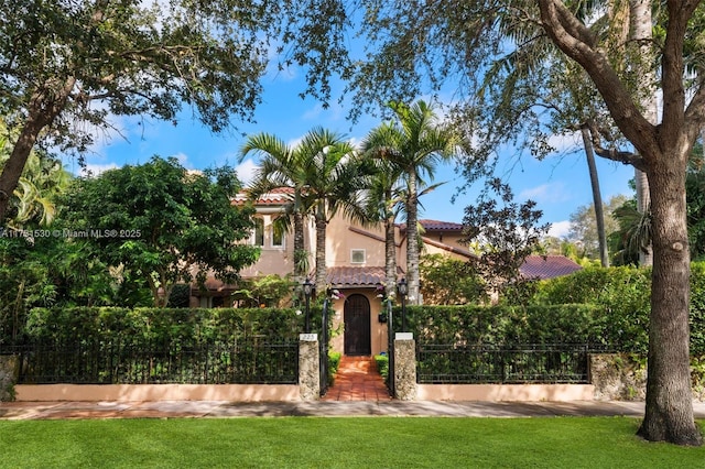 mediterranean / spanish home with a fenced front yard, a tile roof, a gate, and stucco siding