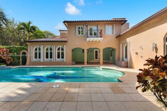 rear view of property featuring a balcony, a patio area, an outdoor pool, and stucco siding