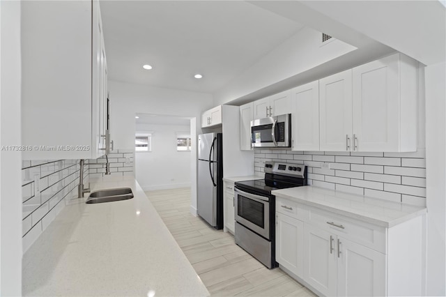 kitchen with sink, white cabinetry, light stone counters, stainless steel appliances, and backsplash