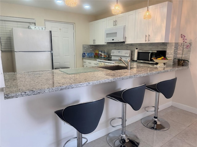 kitchen with a kitchen bar, white cabinetry, light tile patterned floors, kitchen peninsula, and white appliances