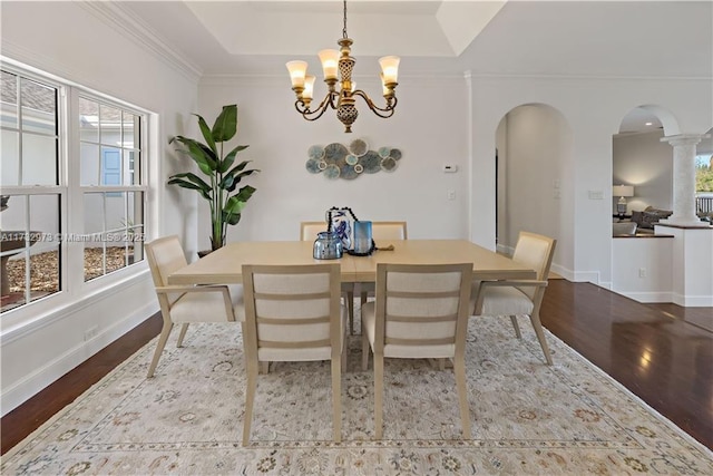 dining room with baseboards, arched walkways, a raised ceiling, wood finished floors, and crown molding