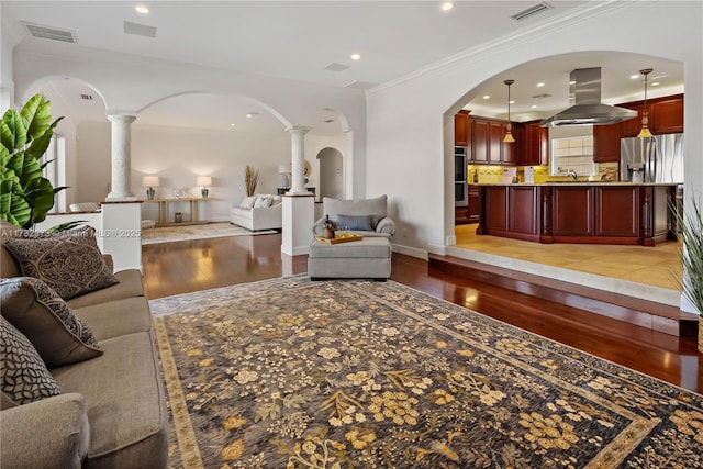 living area with light wood-style floors, visible vents, crown molding, and ornate columns