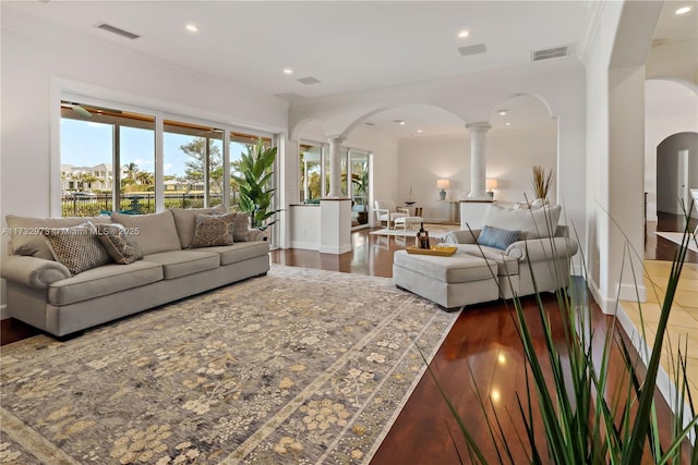 living area featuring arched walkways, visible vents, decorative columns, and wood finished floors