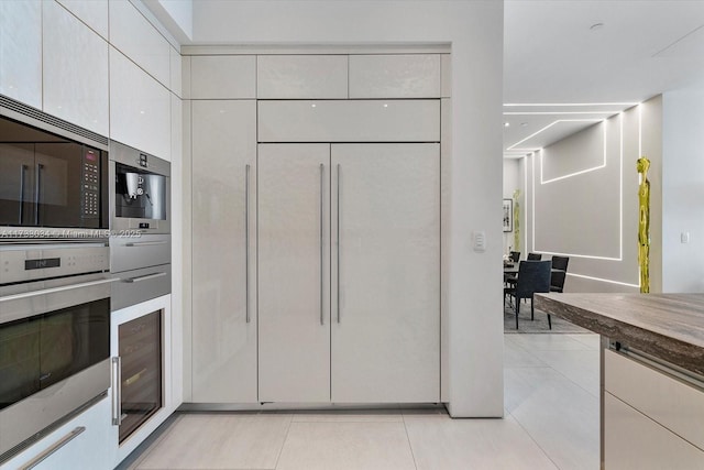 kitchen with white cabinets, stainless steel microwave, beverage cooler, and light tile patterned floors