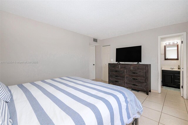 bedroom featuring light tile patterned floors, a closet, a textured ceiling, and ensuite bathroom