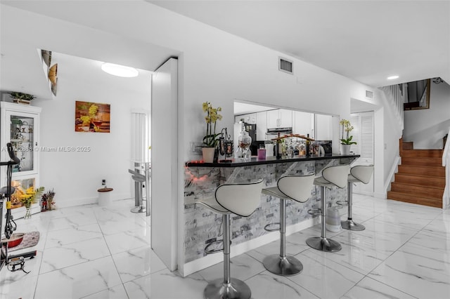 bar with white cabinetry, fridge, and range hood