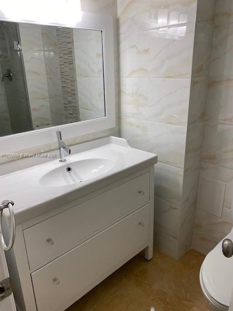 bathroom with vanity, a shower, toilet, and tile walls