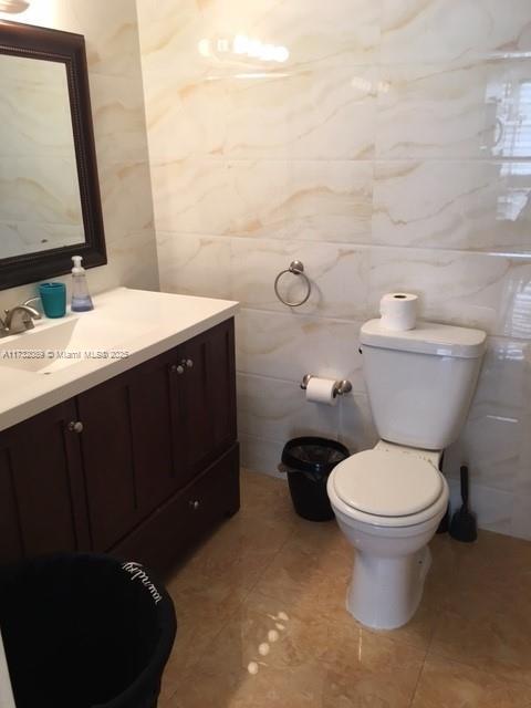 bathroom featuring tile patterned flooring, vanity, tile walls, and toilet