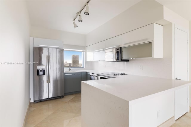 kitchen with stainless steel appliances, light countertops, a sink, modern cabinets, and a peninsula