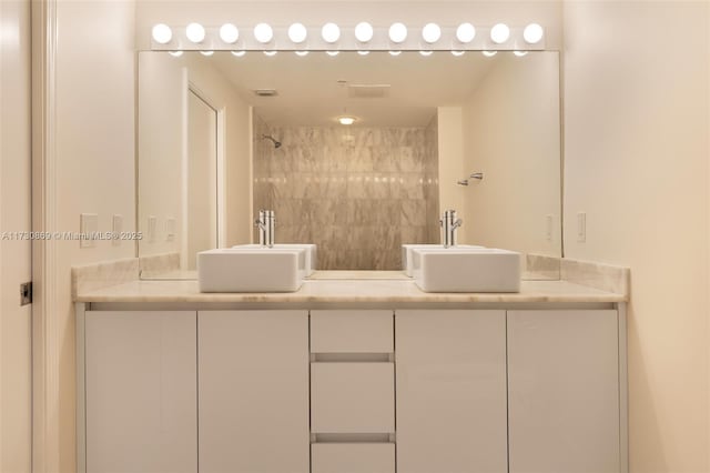 full bathroom with a tile shower, double vanity, a sink, and visible vents