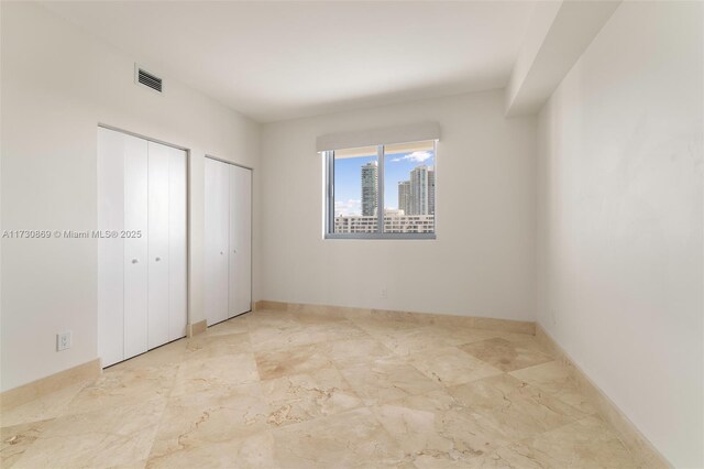unfurnished bedroom with two closets, baseboards, and visible vents