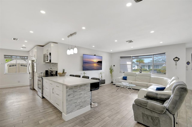 kitchen featuring appliances with stainless steel finishes, decorative light fixtures, a breakfast bar area, white cabinets, and kitchen peninsula