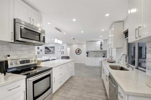 kitchen with sink, white cabinetry, hanging light fixtures, stainless steel appliances, and light stone countertops