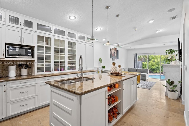 kitchen with lofted ceiling, sink, white cabinetry, pendant lighting, and a kitchen island with sink