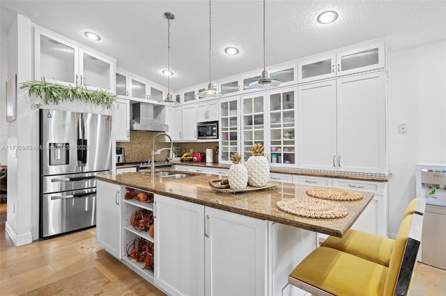 kitchen featuring built in microwave, an island with sink, stainless steel fridge, and dark stone counters