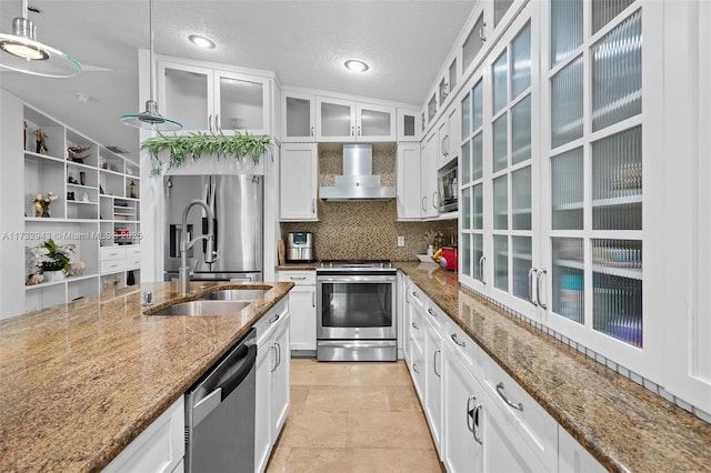 kitchen with wall chimney exhaust hood, white cabinetry, hanging light fixtures, dark stone countertops, and appliances with stainless steel finishes