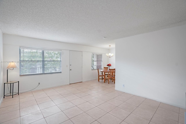 tiled spare room with a textured ceiling, a chandelier, and a healthy amount of sunlight