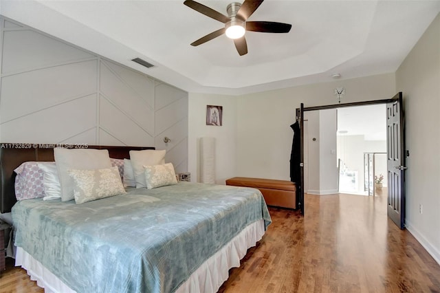 bedroom with ceiling fan, wood-type flooring, and a tray ceiling