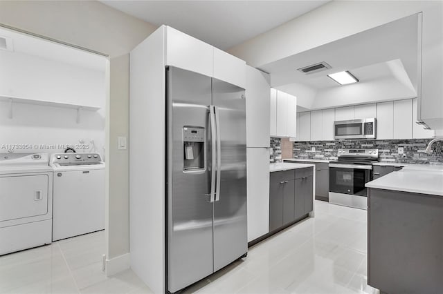 kitchen with white cabinetry, appliances with stainless steel finishes, light tile patterned floors, and washing machine and clothes dryer