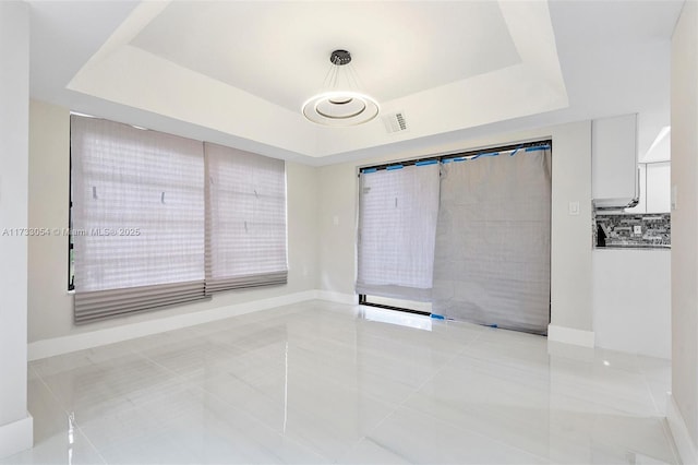 empty room featuring a raised ceiling and light tile patterned flooring