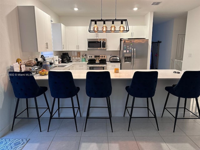 kitchen featuring a breakfast bar area, appliances with stainless steel finishes, white cabinetry, light tile patterned flooring, and decorative light fixtures