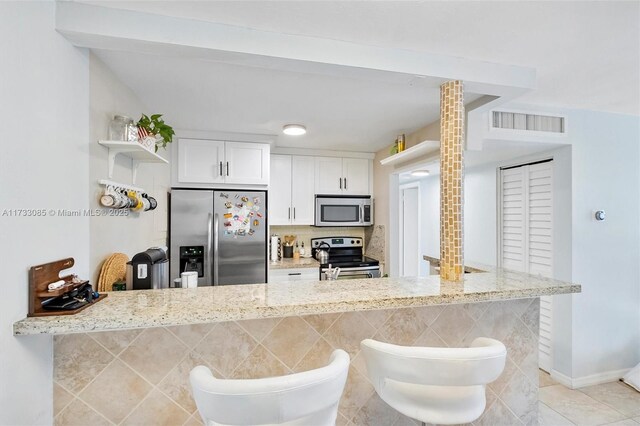 kitchen featuring visible vents, appliances with stainless steel finishes, light tile patterned flooring, white cabinets, and open shelves