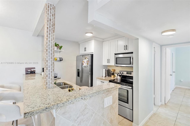 kitchen with a sink, tasteful backsplash, stainless steel appliances, a peninsula, and light stone countertops