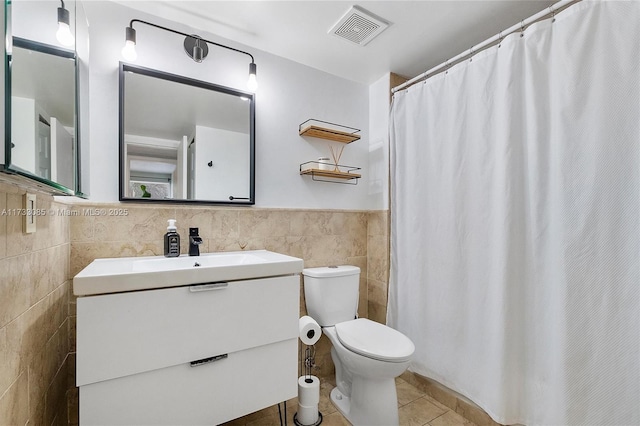 bathroom with visible vents, toilet, vanity, tile patterned floors, and tile walls