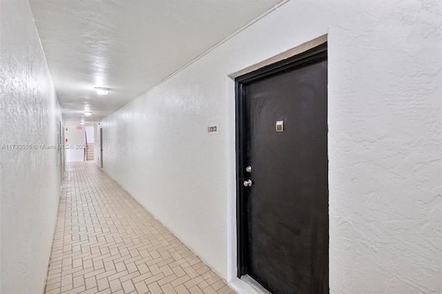 hall featuring light tile patterned flooring and a textured wall