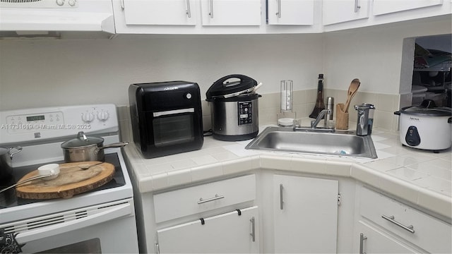 kitchen featuring white cabinets, electric stove, tile countertops, under cabinet range hood, and a sink