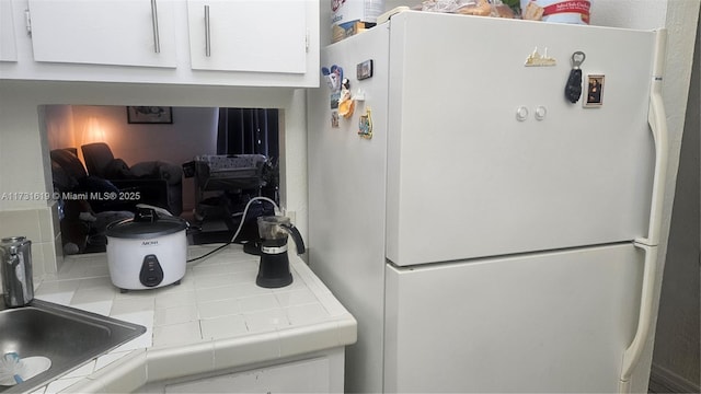 kitchen with tile countertops, white cabinetry, and freestanding refrigerator