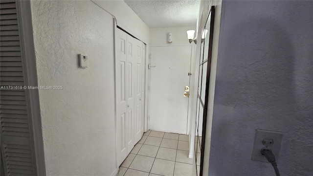 hall with a textured ceiling, a textured wall, and light tile patterned flooring