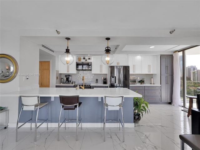 kitchen featuring a breakfast bar area, hanging light fixtures, appliances with stainless steel finishes, white cabinets, and backsplash