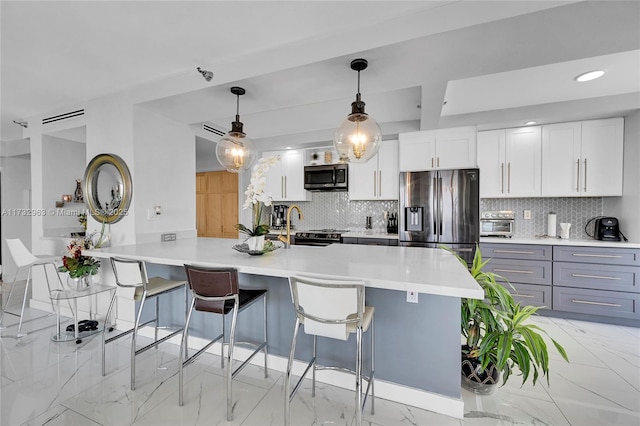 kitchen featuring white cabinetry, hanging light fixtures, appliances with stainless steel finishes, a kitchen breakfast bar, and decorative backsplash