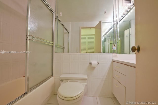 full bathroom featuring combined bath / shower with glass door, tile walls, tile patterned flooring, vanity, and toilet