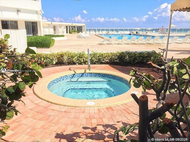 view of pool featuring a hot tub, a water view, and a patio area