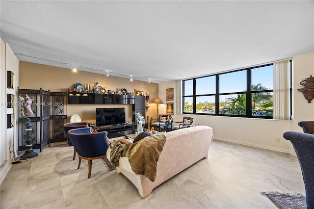 living area with a textured ceiling, marble finish floor, track lighting, and baseboards