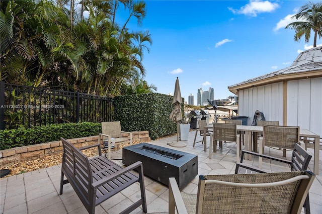 view of patio with a fire pit, a view of city, outdoor dining space, and fence