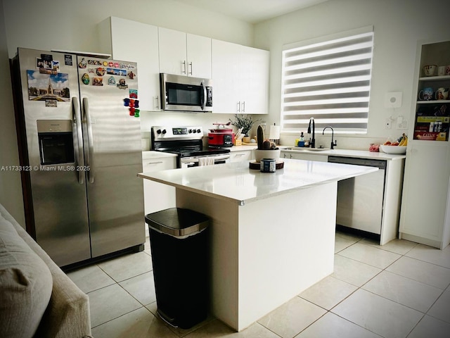 kitchen featuring sink, light tile patterned floors, appliances with stainless steel finishes, a kitchen island, and white cabinets