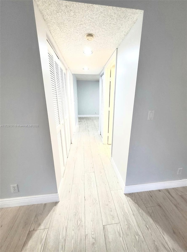 corridor featuring light wood-type flooring and a textured ceiling