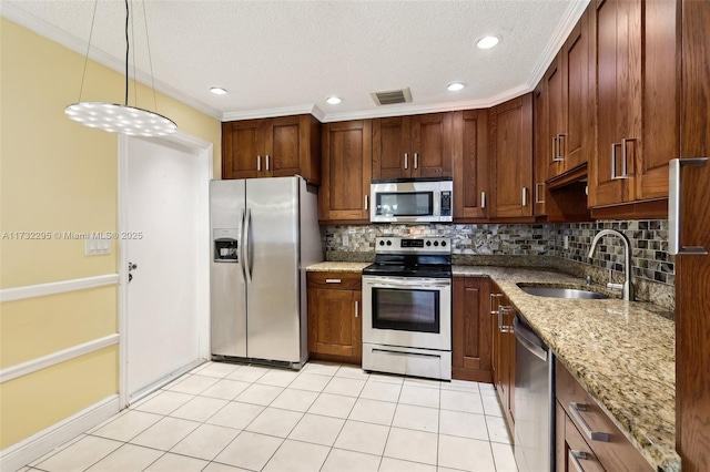 kitchen with appliances with stainless steel finishes, decorative light fixtures, sink, decorative backsplash, and light stone countertops