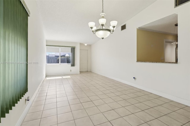 empty room with light tile patterned floors, a textured ceiling, and a chandelier