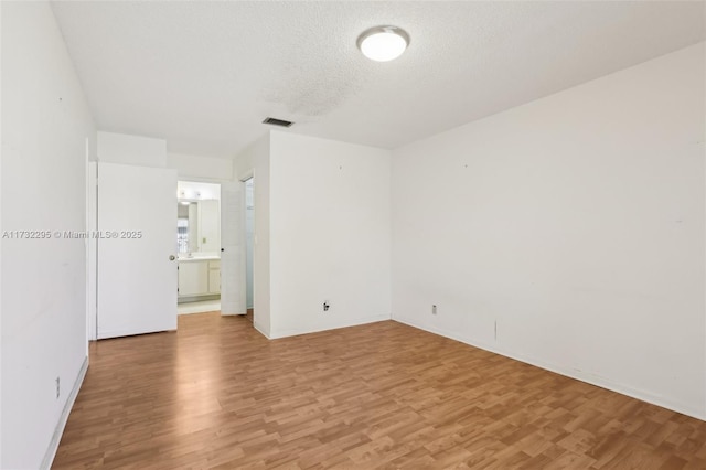 spare room featuring light hardwood / wood-style floors and a textured ceiling