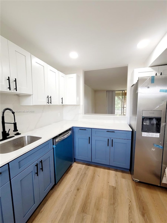 kitchen with appliances with stainless steel finishes, sink, white cabinets, decorative backsplash, and light wood-type flooring